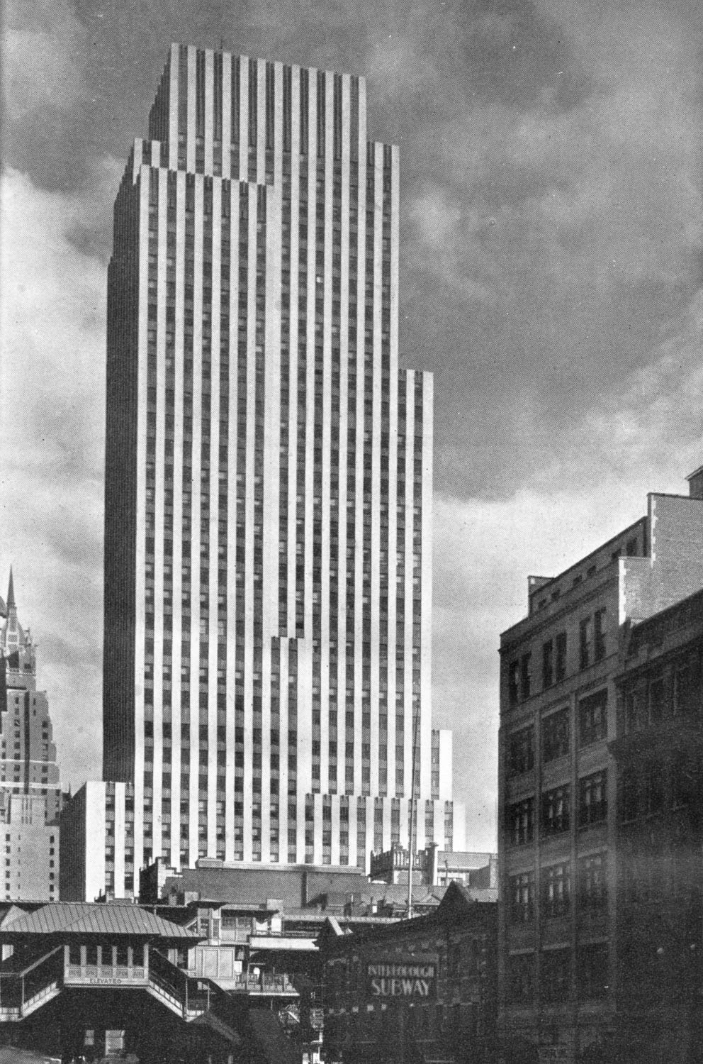 A black and white photograph of a skyscraper taken from street level a few blocks away. The facade of the building is made up of thin alternating bands of light and dark. The bands are continuous, running from the lower portion of the building all the way to the top. There is no ornament at the top of the building; the bands end where the building does. The building is a large slab, similar to the proportions of a cereal box, and only has a few, very small setbacks.
